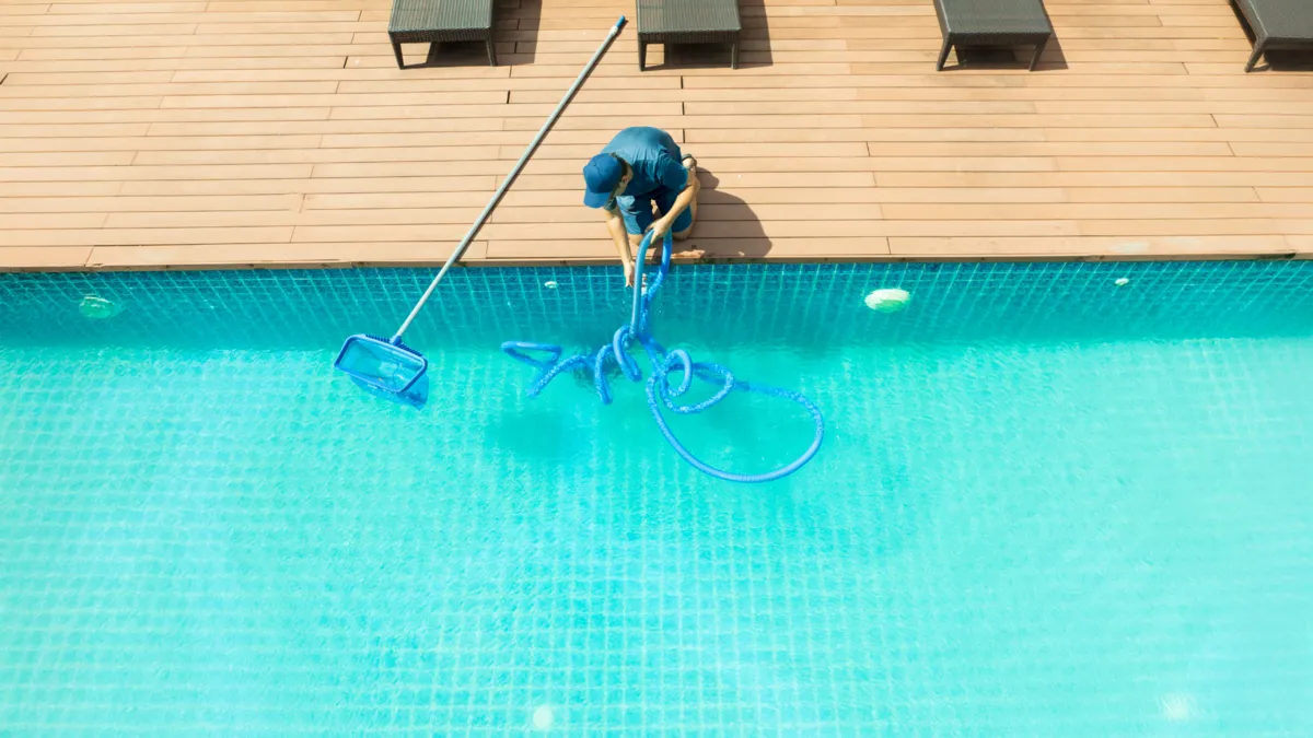 Local service worker cleaning a swimming pool on a customer property